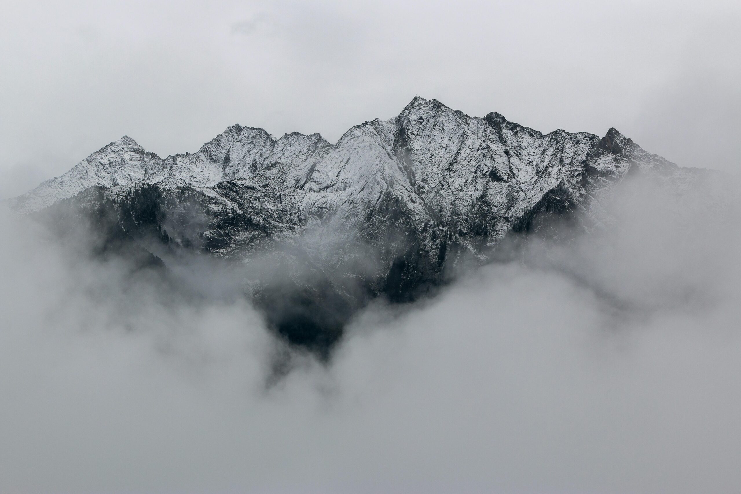 A breathtaking view of snow-covered mountain peaks surrounded by dense fog, creating a mystical landscape.